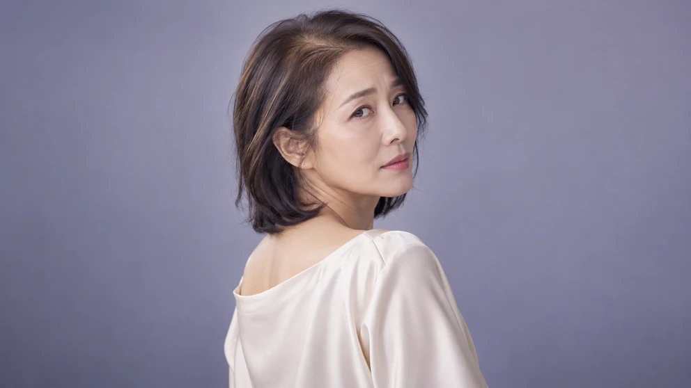 어깨 너머로 고개를 돌린 중년 여성의 쇄골 길이 소프트 블랙 중단발과 목선표 이미지 방향: 고개를 돌려 착용감을 확인하는 순간. 뒤에서 비스듬히 잡아 중단발 옆선과 목선의 연결이 보이게, 그레이시 라벤더 단색 배경